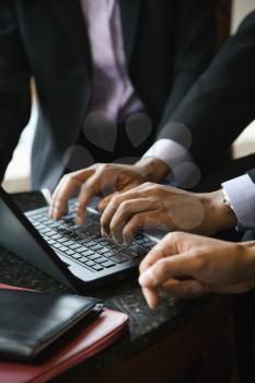 Cropped close-up of three business people and a laptop with the focus on hands typing in the foreground. Vertical format.