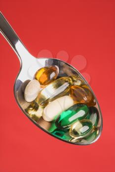 Silver spoon with different types of pills. Vertical shot. Isolated on red.