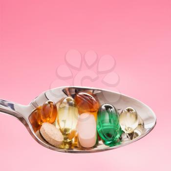 Silver spoon with different types of pills. Square format. Isolated on pink.