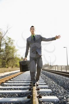 Young businessman with a briefcase balances on railroad tracks. Vertical shot.