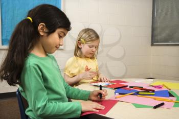 Two young girls in classroom creating art. Horizontally framed shot.