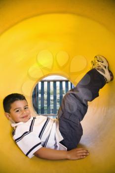 Young boy lying in crawl tube at playground. Vertically framed shot.