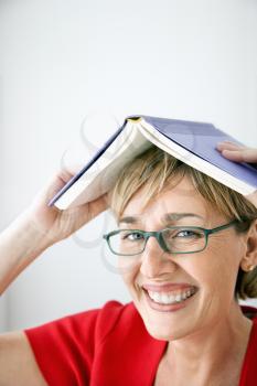 Woman smiling holding book on head. 