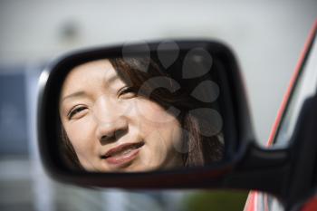 Reflection of Asian woman in side  view car mirror smiling.