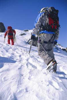 Two mountain climbers walking up snowy mountain (selective focus)