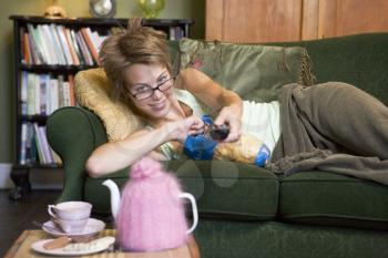 Royalty Free Photo of a Woman Lying on a Couch Holding a Remote and Eating Potato Chips