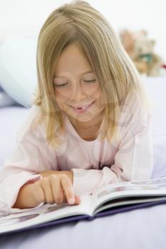 Royalty Free Photo of a Girl Lying on Her Bed Reading a Book