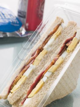 Royalty Free Photo of an Egg And Bacon Sandwich On White Bread With A Bag Of Crisps And A Can Of Fizzy Drink