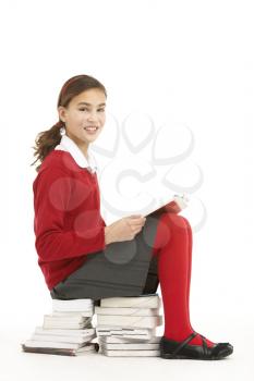 Female Student In Uniform Sitting On Pile Of Books Reading