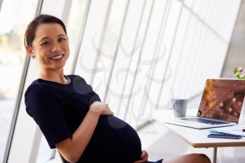Portrait Of Pregnant Businesswoman Using Laptop In Office