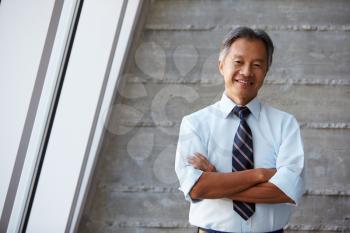 Asian Businessman Standing Against Wall In Modern Office