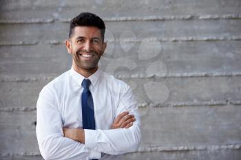Hispanic Businessman Standing Against Wall In Modern Office