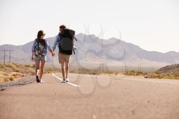 Rear View Of Couple On Vacation Hitchhiking Along Road