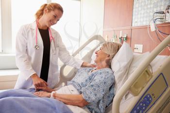 Female Doctor Talks To Senior Female Patient In Hospital Bed