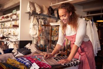 Female Sales Assistant Arranging Textiles In Homeware Store