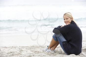 Young Woman On Holiday Sitting On Winter Beach