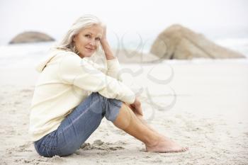 Senior Woman On Holiday Sitting On Winter Beach