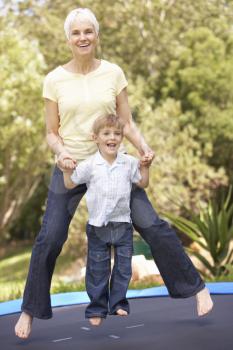 Grandmother And Grandson Jumping On Trampoline In Garden