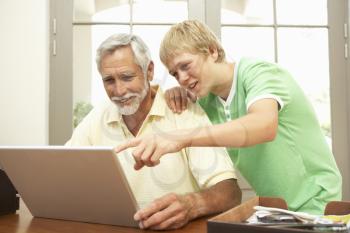 Teenage Grandson Helping Grandfather To Use Laptop At Home