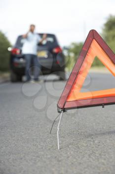 Driver Broken Down On Country Road With Hazard Warning Sign In Foreground