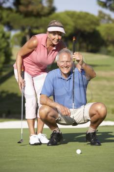 Senior Couple Golfing On Golf Course Lining Up Putt On Green