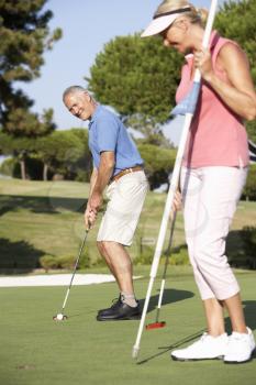 Senior Couple Golfing On Golf Course Lining Up Putt On Green