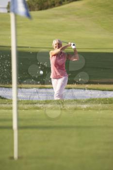 Senior Female Golfer Playing Bunker Shot On Golf Course