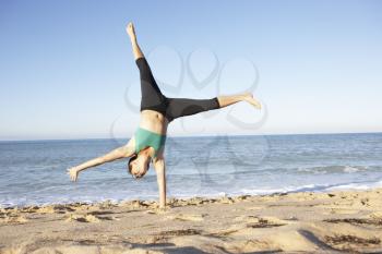 Young Woman In Fitness Clothing Turning Cartwheel On Beach