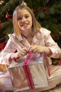 Young Girl Opening Christmas Present In Front Of Tree
