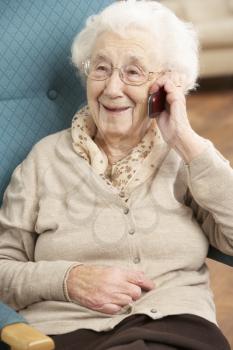 Senior Woman Talking On Mobile Phone Sitting In Chair At Home