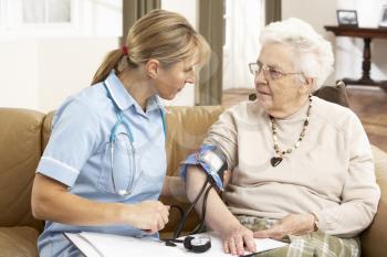 Senior Woman Ihaving Blood Pressure Taken By Health Visitor At Home