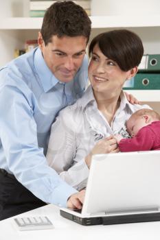 Parents With Newborn Baby Working From Home Using Laptop
