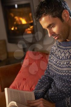 Middle Aged Man Relaxing With Book By Cosy Log Fire