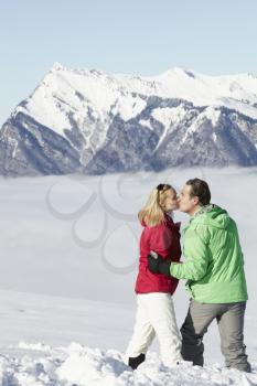 Couple Admiring Mountain View Whilst On Ski Holiday In Mountains