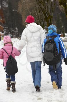 Mother Walking Two Children To School Along Snowy Street In Ski Resort