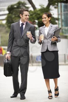 Businessman And Businesswoman Walking Along Street Holding Takeaway Coffee