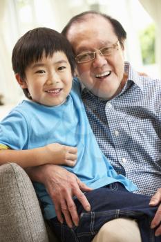 Chinese Grandfather And Grandson Relaxing On Sofa At Home