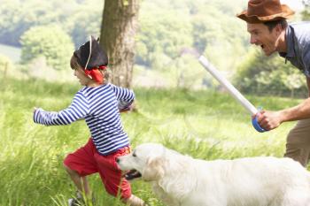 Father Playing Exciting Adventure Game With Son And Dog In Summer Field