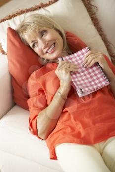 Senior Woman Sitting On Sofa Reading Diary