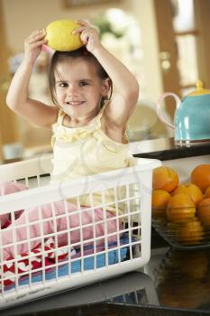 Girl Sitting In Laundry Basket On Kitchen Counter With Lemon