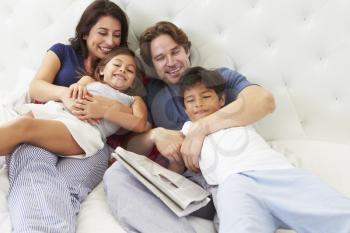 Family Relaxing In Bed With Coffee And Newspaper