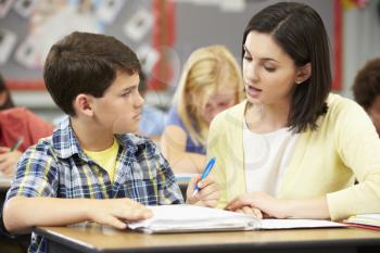 Teacher Helping Pupils Studying At Desks In Classroom