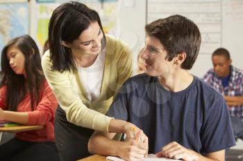 Teacher Helping Male Pupil Studying At Desk In Classroom
