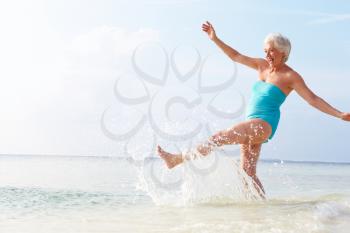 Senior Woman Splashing In Sea On Beach Holiday
