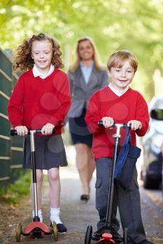 Children Riding Scooters On Their Way To School With Mother