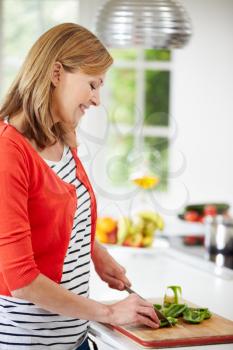 Woman Standing At Counter Preparing Meal In Kitchen