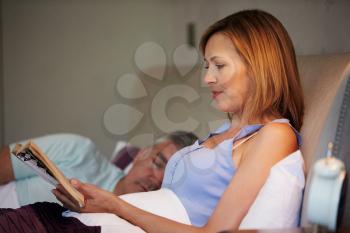 Middle Aged Couple In Bed Together With Woman Reading Book
