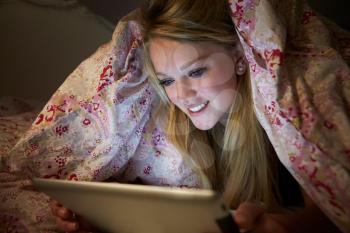 Teenage Girl Using Digital Tablet In Bed At Night