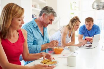 Teenage Family Having Breakfast In Kitchen With Laptop