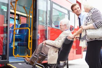 Driver Helping Senior Couple Board Bus Via Wheelchair Ramp
